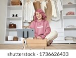 Happy hipster gen z teen girl fashion social media channel blogger with pink hair wear hoodie recording unboxing vlog on phone video camera tutorial sit on floor with online store clothes order box.