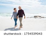 Senior couple walking and looking at each other at beach. Happy mature couple in love walking barefoot at sea shore. Loving retired man with beautiful woman relaxing at the ocean with copy space.