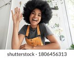 Pretty young African American mixed race hipster vlogger woman with Afro hair waving hand looking at webcam talking to camera sits at cafe table video calling, recording blog, headshot portrait.