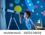 Curious boy using telescope to explore moon surface at night in his bedroom. Young child using telescope to see remote galaxy from room with decorated wall with rocket, planets, stars and spaceship.