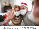 Front view of senior couple with face masks indoors at home at Christmas, taking selfie.