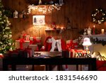 Santa Claus costume and hat hanging on chair at table with Merry Christmas decor gifts presents on holiday eve in cozy Santa home workshop interior late in night with light on xmas tree and fireplace.