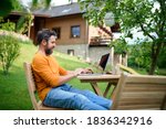 Side view of man with laptop working outdoors in garden, home office concept.