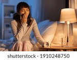 people, bedtime and rest concept - sleepy asian woman with clock yawning in bed at night