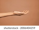 Beautiful woman hand isolated on brown background. Empty open female hand on cream background with copy space. Close up of elegant palm faced upwards with space for your product.