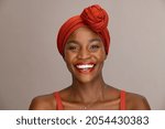 Portrait of beautiful african woman with red headscarf against brown background with copy space. Cheerful black mid woman wearing ethnicity headband. Mature happy lady with traditional clothes.