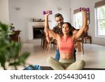 Small photo of Middle aged man helping ethnic woman working with dumbbells at home. Black fit woman with her personal fitness trainer exercising with weights. Multiethnic girl doing chest and shoulder dumbbell press