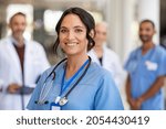 Portrait of happy young nurse in uniform with healthcare team in background. Successful team of doctor and nurses smiling. Beautiful and satisfied healthcare worker in private clinic looking at camera