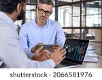 Small photo of Diverse managers traders analysts discussing financial growth market at desk with laptop with graphs on screen using tablet device. Investors brokers analysing indexes online cryptocurrency stock.