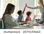 Small photo of Happy smiling Caucasian female teacher giving high five to asian schoolboy standing in classroom with group of schoolchildren. Teamwork successful lesson. Technologies for education concept.