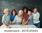 Small photo of Portrait of cheerful smiling teacher and diverse schoolchildren standing posing on chalkboard blackboard background looking at camera happy after school reopen on mathematics lesson. Diversity.