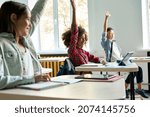 Small photo of Happy diligent smiling multiethnic diverse schoolchildren having lesson at elementary stem class sitting at desks using gadgets. Schoolkids raising hands answering to questions at workplace.