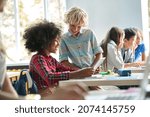 Small photo of Happy smiling Caucasian boy and African American girl schoolchildren studying together using tablet device in classroom. Groups of schoolchildren working on task. Technologies for education concept.