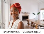 Portrait of a beautiful african woman smiling while looking at camera. Mid adult woman with traditional african headscarf stay at home and smiling. Cheerful mature lady standing near the window.