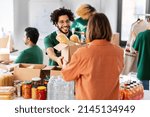 Small photo of charity, donation and volunteering concept - happy smiling male volunteer giving box of food to woman at distribution center at distribution or refugee assistance center