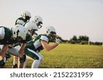Small photo of Group of young American football players going over offensive drills on a sports field during a team practice