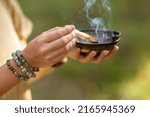 Small photo of occult science and supernatural concept - close up of woman or witch with smoking palo santo stick and bowl performing magic ritual in forest
