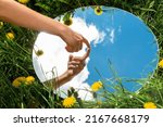 Small photo of nature concept - hand touching sky reflection in round mirror on summer field