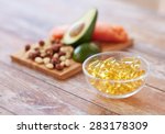 healthy eating, diet and omega 3 nutritional supplements concept - close up of cold liver oil capsules in glass bowl and food on table