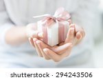 Close up shot of female hands holding a small gift wrapped with pink ribbon. Small gift in the hands of a woman indoor. Shallow depth of field with focus on the little box.