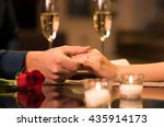 Closeup of couple hands on restaurant table with two glasses of champagne. Romantic couple holding each other's hand at dinner in a luxury restaurant. Marriage proposal and engagement concept.
