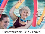 Smiling senior woman doing aqua fitness with swim noodles. Happy mature healthy woman taking fitness classes in aqua aerobics. Healthy old woman holding swim noodles doing aqua gym with young trainer.
