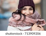 Closeup face of a young happy woman enjoying winter wearing scarf and cap. Smiling girl in a colorful shawl looking at camera. Latin woman with knitted bordeaux hat and woolen scarf.