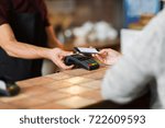 modern technology and people concept - man or bartender with payment terminal and customer with smartphone at bar of coffee shop