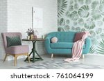 Green table with a plant between pink chair and blue sofa in floral living room with wallpaper and poster