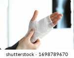 Small photo of Close-up of persons hand wrapped in white ace bandage. Fracture bone and x ray image. Injured wrist in accident. Hospital help and recovery. Modern medicine concept