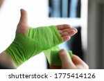 Small photo of Close-up of person ties up hand with green ace bandage. Fracture bone and x ray image of break wrist. Injury or accident. Modern medicine and long recovery concept