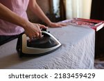 Close-up of female housewife ironing crumpled bedsheet on board using steam iron. Woman doing housework. Housekeeping and household chores concept