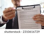 Small photo of Smiling manager shows contract on clipboard to partner in office. Businessman offers to read agreement documents before signification