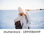 back view of woman in snowy mountain wearing modern coat at sunset. Holding cute jack russell dog in arms. winter season. nature at sunset