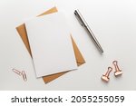 Small photo of Greeting, wedding or congratulations stationery mockup. Blank sheet of paper on brown envelope, fountain pen and various paper clips on clean desk. Table top view, flat lay, copy space.