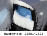 Closeup of a blue-tinted car side mirror covered in snow and water droplets