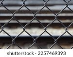 Textured black chain link fence. Abstract closeup with blurred railroad tracks in the background.