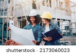 Small photo of Young female architector and engineers with draft plan of building talking on constructing site. Construction manager and engineer working on building site.
