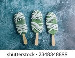 Fun Halloween monsters popsicle. Happy Holiday. Green chocolate popsicles with mastic bandages over dark background. Top view