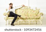 Small photo of Macho sits with open book on head, like roof. Overstudy concept. Man with beard and mustache sits on sofa, white wall background. Guy overdid with studying, fed up of reading old boring book