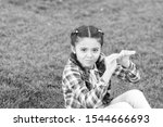 Small photo of Kid gadabout. Girl little kid spend leisure outdoors in park. Girl sit on grass in park. Child enjoy spring sunny weather while sitting at meadow in park. Springtime concept. Park and garden.