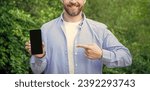 Small photo of man presenting and pointing finger on smartphone screen with copy space. presenting smartphone. man presenting smartphone. man presenting smartphone outdoor