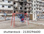 Small photo of KYIV, UKRAINE - Feb. 25, 2022: War of Russia against Ukraine. Child on a swing against a residential building damaged by russian rocket in a residential area of Kyiv. Russian world in Ukraine