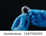 Invisible orthodontics cosmetic aligners in hands of doctor wearing sterile gloves isolated on a black background, tooth aligners, plastic braces. Modern teeth retainers created on a 3d printer.