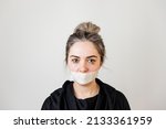 Small photo of violence against women. domestic violence. young frightened woman, sealed mouth with tape, isolated on dark background.silence,limitation of freedom of speech. in the concept of violence against women