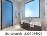 Stylish design of the bathroom in the hotel, with a frosted glass door and a false window. Bath with shower, heated towel rail and bathrobes.