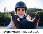 Small photo of Portrait of a happy beautiful white woman in her competition uniform riding her bay horse on a dressage ring with a forest in the background on a sunny day