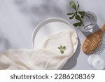 Small photo of A round dish decorated with a white towel, cotton pads, wooden brush and a glass vase with tree branch. Empty space for natural beauty product advertising