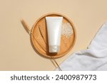 Flat lay of a tube of facial cleanser displayed on a round wooden plate with whole grain rice. Blank labels for branding and advertising. Minimalist background.