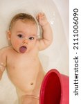 Small photo of Impish baby girl taking bath and makes a face showing her tongue, user-generated aesthetics